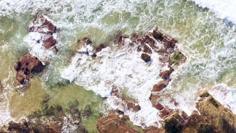 Waves-rolling-from-right-corner-of-frame-onto-sedimentary-ocean-rocks-POV-drone-Turimetta-Beach-Sydney-Australia