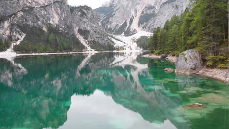 Forward-drone-shot-around-a-male-model-standing-on-a-rock-overlooking-lake-Braies-in-the-Dolomites,-Italy
