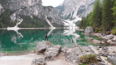 Circular-drone-shot-around-a-male-model-standing-on-a-rock-overlooking-lake-Braies-in-the-Dolomites,-Italy