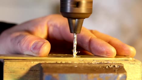 Slow-motion-footage-of-craftsman-drilling-brass-sheet-with-man's-hand-holding-brass