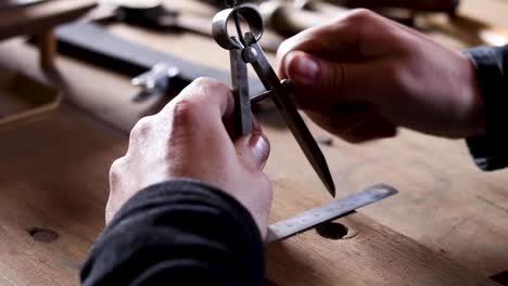 Close-up-of-man-adjusting-steel-measuring-compass-with-ruler-on-vintage-wooden-bench-in-workshop