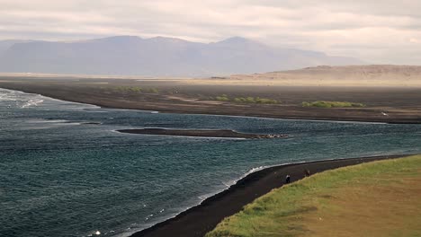 Some-people-walk-on-a-black-sand-beach-on-the-Icelandic-coastline