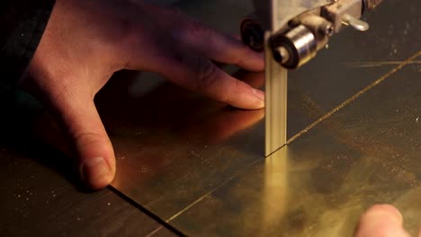 Close-up-footage-of-cutting-brass-metal-with-band-saw-with-man's-hand-pushing-sheet-of-brass-through-saw