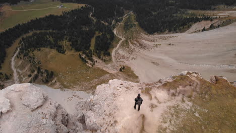 Aerial-shot-from-drone-passing-an-young-model-standing-on-the-edge-of-a-rock-overlooking-valley-in-the-Dolomites,-Italy