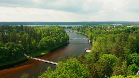 Aerial-view-of-a-green-forests,-a-river-a-pedestrian-bridges-in-Latvia