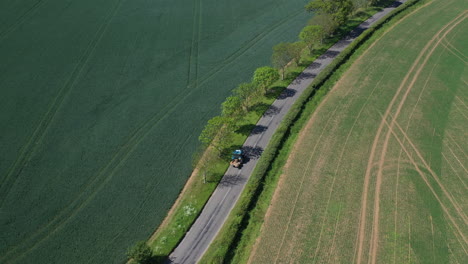 Aerial-shot-of-a-small-blue-tractor-driving-down-the-road