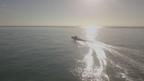 Slow-motion-aerial-drone-footage-of-motor-boat-travelling-towards-sun-and-then-turning-at-high-speed-across-smooth-ocean-water