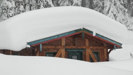 Small-hut-with-masses-of-snow-on-the-roof-during-snowfall,-zooming-in
