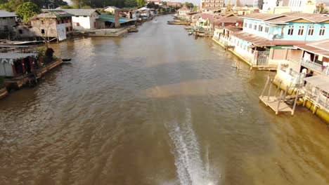 Barco-Conduciendo-Por-El-Río-En-Nyaung-Shwe-Myanmar-En-El-Lago-Inle,-Edificios-Tradicionales-En-Segundo-Plano