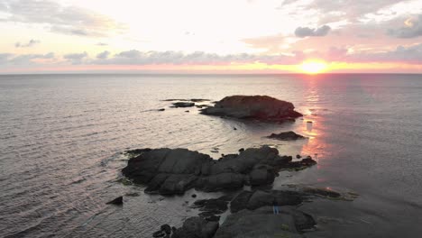 Aerial-shot-from-drone-over-an-young-man-enjoying-the-sunrise-on-rocks-in-the-sea-near-Lozenets,-Bulgaria