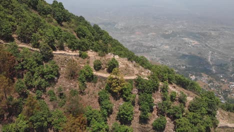 Aerial-circular-shot-from-a-drone-of-an-young-man-enjoying-the-view-of-Kathmandu-from-a-hiking-trail,-Nepal