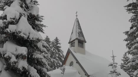 Chapel-covered-with-snow-surrounded-by-trees,-medium-tilt-down-shot