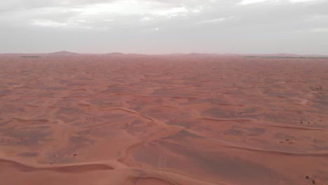 Flying-backwards-aerial-shot-of-arabian-red-desert-dunes-at-sunset-in-Dubai,-United-Arab-Emirates