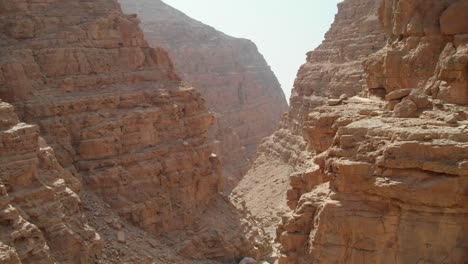 Bird's-eye-view-from-drone-going-through-rocky-valleys-in-desert-mountains,-United-Arab-Emirates