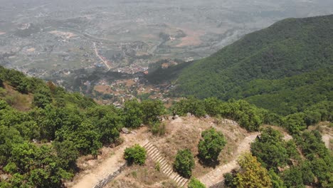 Aerial-revealing-shot-from-a-drone-of-an-young-man-enjoying-the-view-of-Kathmandu-from-a-hiking-trail,-Nepal