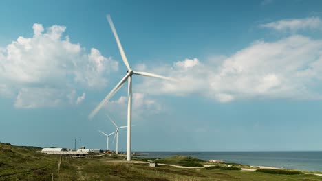 Zeitraffer-Von-Windkraftanlagen,-Die-Sich-Schnell-An-Der-Küste-Des-Meeres-Mit-Blauem-Himmel-Und-Sich-Bewegenden-Wolken-Drehen