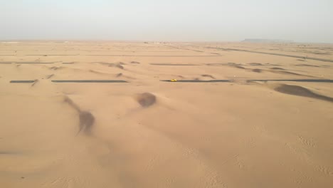 Luftrundschuss-Mit-Einer-Drohne-Eines-Sportwagens-Inmitten-Von-Mit-Sand-Bedeckten-Wüstenstraßen-In-Dubai,-Vereinigte-Arabische-Emirate