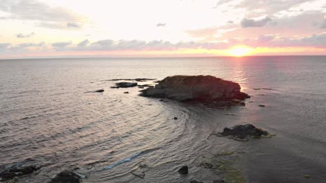 Aerial-shot-from-drone-over-an-young-man-enjoying-the-sunrise-on-rocks-in-the-sea-near-Lozenets,-Bulgaria