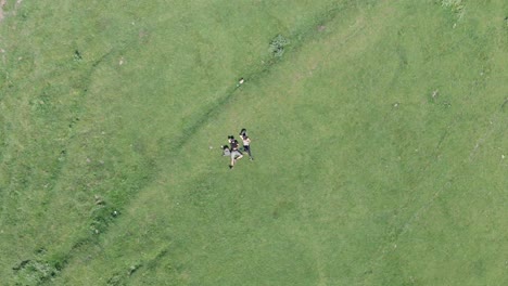 Aerial-view-of-young-couple-laying-down-on-a-grass-and-relaxing-after-exhausting-hike-to-Gergeti-Trinity-Church,-Georgia