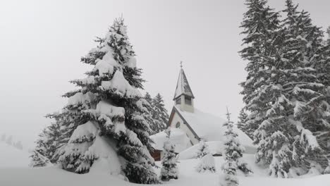 Chapel-covered-with-snow-surrounded-by-trees,-wide-angle-panning-shot