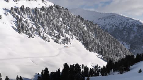 Isoliertes-Schneebedecktes-Chalet-In-Schneebedeckten-Bergen-Mit-Bäumen-Und-Blauem-Himmel,-Herauszoomen