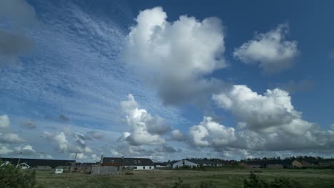 Timelapse-of-clouds-moving-in-a-blue-sky-over-houses-with-gras-and-trees-in-foregorund