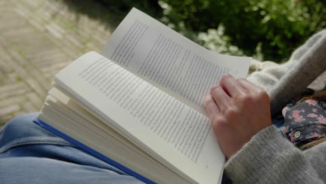 Close-up-open-book-as-young-woman-reads-in-garden,-dutch-angle