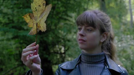 Young-woman-stares-at-golden-leaf-in-hand-in-woods,-close-up