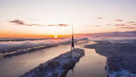 Aerial-hyperlapse-over-a-river-and-tv-tower-at-sunrise-on-a-cold-early-winter-morning