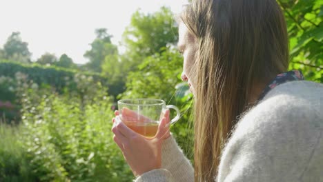 Young-woman-long-hair-enjoys-tea-in-bright-green-garden,-over-shoulder