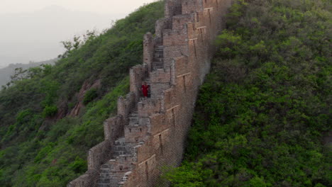 Eine-Person-In-Rot-Steigt-Die-Stufen-Einer-Langen-Steinmauer-Hinauf,-Die-über-Den-Berg-Führt