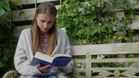 Young-woman-reads-book-on-bench-in-garden,-medium