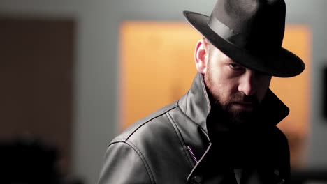 Man-in-hat-and-black-jacket-looks-into-camera-and-pulls-himself-into-jacket