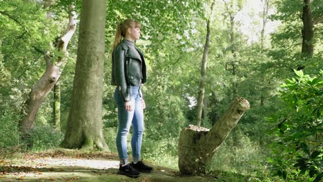 Stylish-young-woman-stands-next-to-stump-in-bright-forest,-full