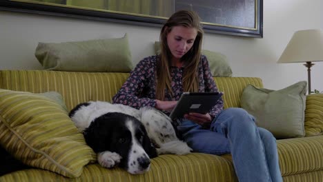 Young-woman-sits-reading-table-on-couch-with-pet-dog