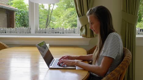 Girl-sits-at-table-indoors-working-on-laptop,-slider
