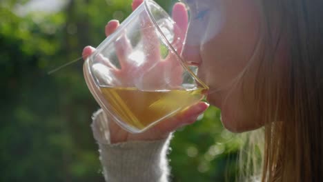 Girl-drinks-tea-from-glass-outside-in-garden,-lens-flare,-close-up