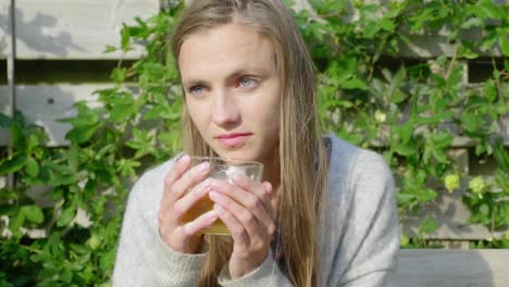 Girl-with-bright-eyes-enjoys-tea-outside-in-warm-sunlight,-close-up