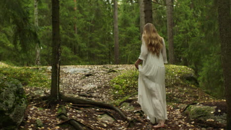 A-woman-in-a-long-white-dress-walks-through-a-forest