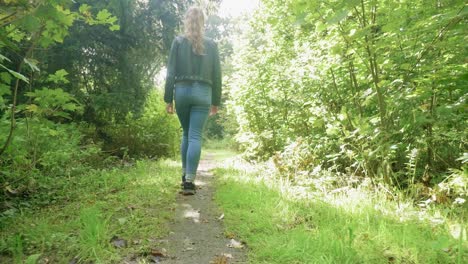 Following-girl-walking-along-path-through-woods-in-sunlight,-low-angle