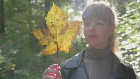 Girl-gazes-at-sunlight-glowing-through-golden-leaf-in-forest