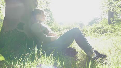 Girl-rests-against-trunk-of-tree-in-warm-sunlight,-lens-flare