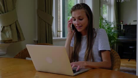 Young-attractive-woman-calls-while-working-on-a-laptop-sitting-at-a-table,-slow-motion