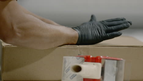 Person-wearing-gloves-seals-cardboard-box-with-tape