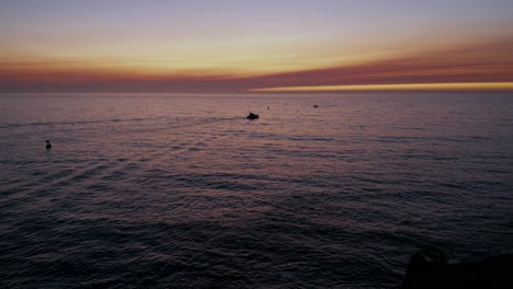 Two-silhouetted-boats-in-the-ocean-at-sunset