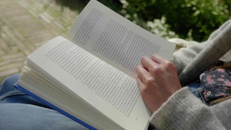 Slow-motion-close-up-shot-of-a-book-being-read-and-by-a-young-woman-sitting,-turning-a-page