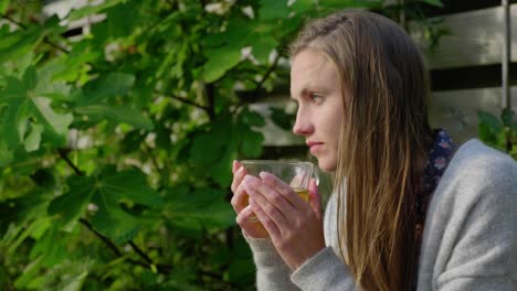 Girl-with-long-hair-sits-outside-enjoying-tea-and-staring-out,-medium