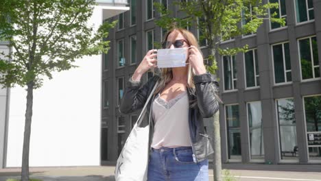 Hübsche-Blonde-Frau-Mit-Dunkler-Sonnenbrille,-Die-In-Amsterdam,-Niederlande,-Eine-Gesichtsmaske-Aufsetzt