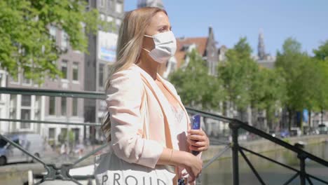 Charming-Woman-Wearing-Mask,-Waiting-For-Someone-At-The-Bridge-Over-Amsterdam-Canal-In-Netherlands---medium-shot