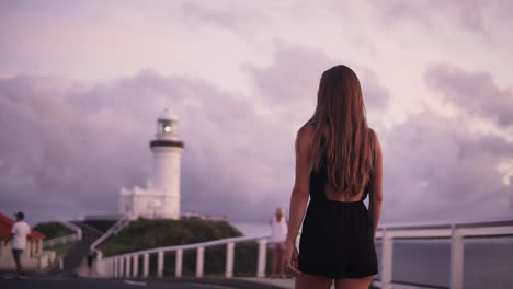 Female-walking-towards-lighthouse-in-vibrant-sunrise